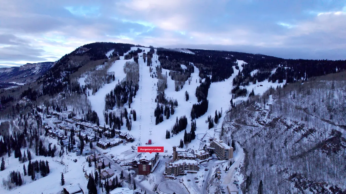 A sweeping exterior view of Purgatory Lodge set against the ski slopes and snow-covered pine forests, with the mountains rising in the background. The image exudes a sense of adventure and tranquility, showcasing direct access to world-class winter sports right outside the lodge.