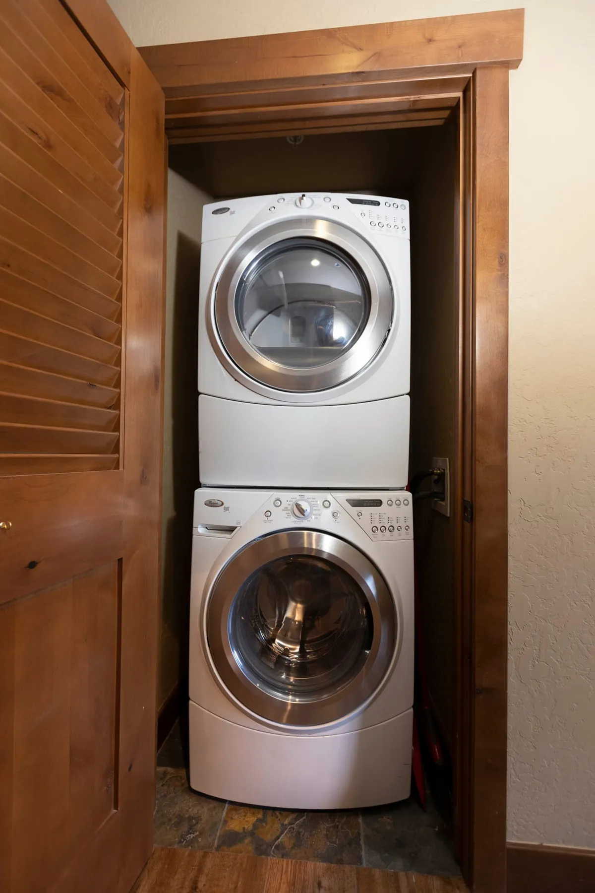A compact, efficient laundry area featuring a stacked washer and dryer tucked behind a wooden door, set against textured walls. The setup underscores the convenience of in-unit laundry for guests preparing for adventure.