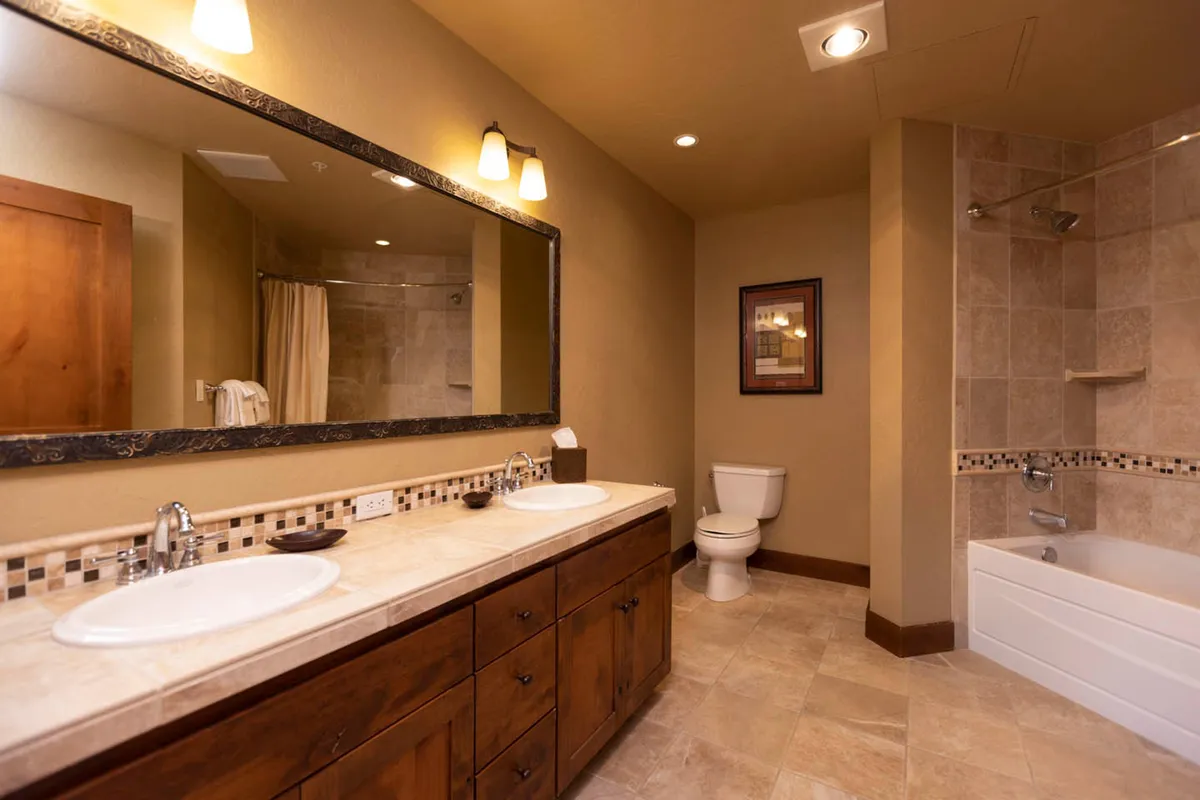 A spacious, serene bathroom with a double sink vanity, large mirror, bathtub, and framed artwork. The overall ambiance is tranquil and organized, ideal for unwinding privately in the master suite's en-suite bath.