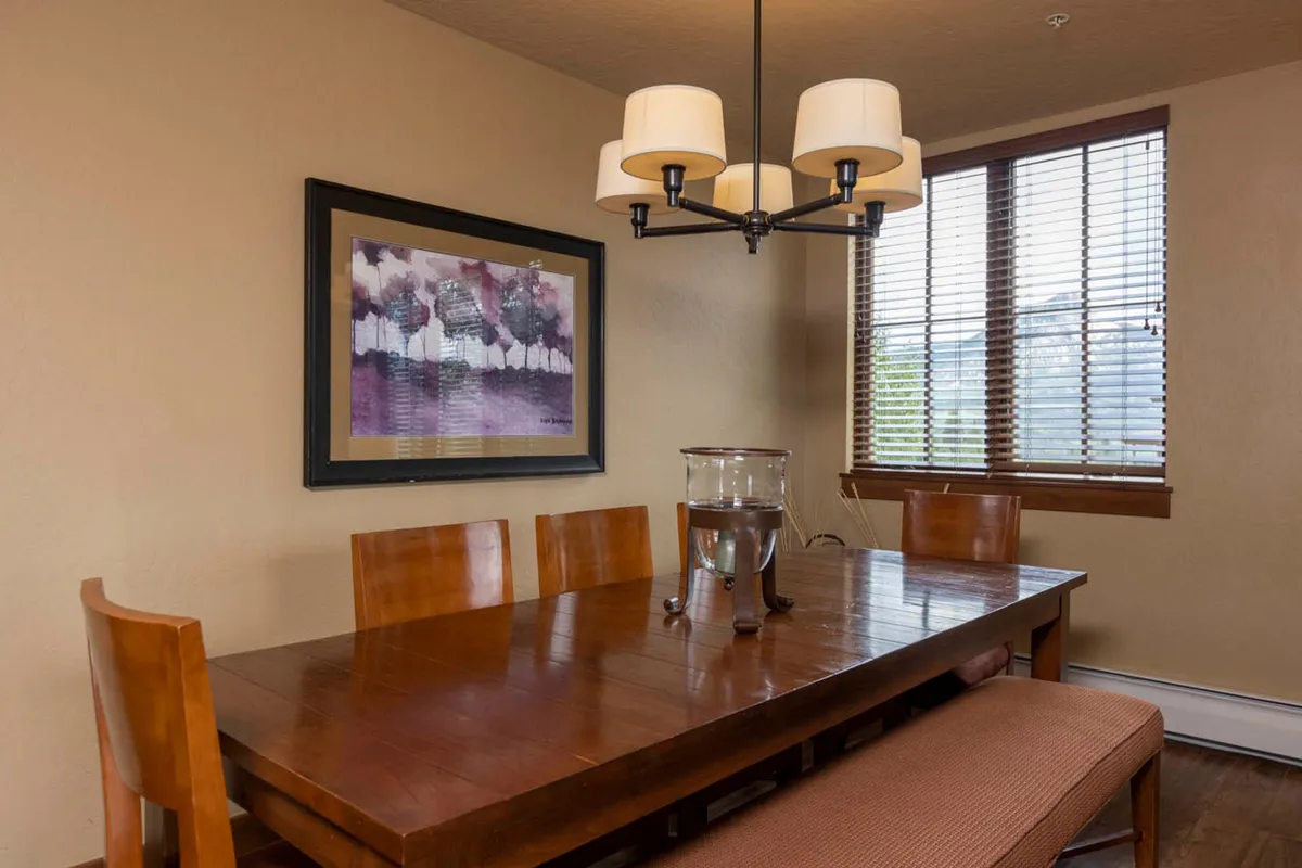 A cozy dining area with a wooden table set beneath a chandelier, framed by artwork and soft natural light. The table is large enough for group dinners or relaxed brunches, embodying a space designed for connection and conversation.