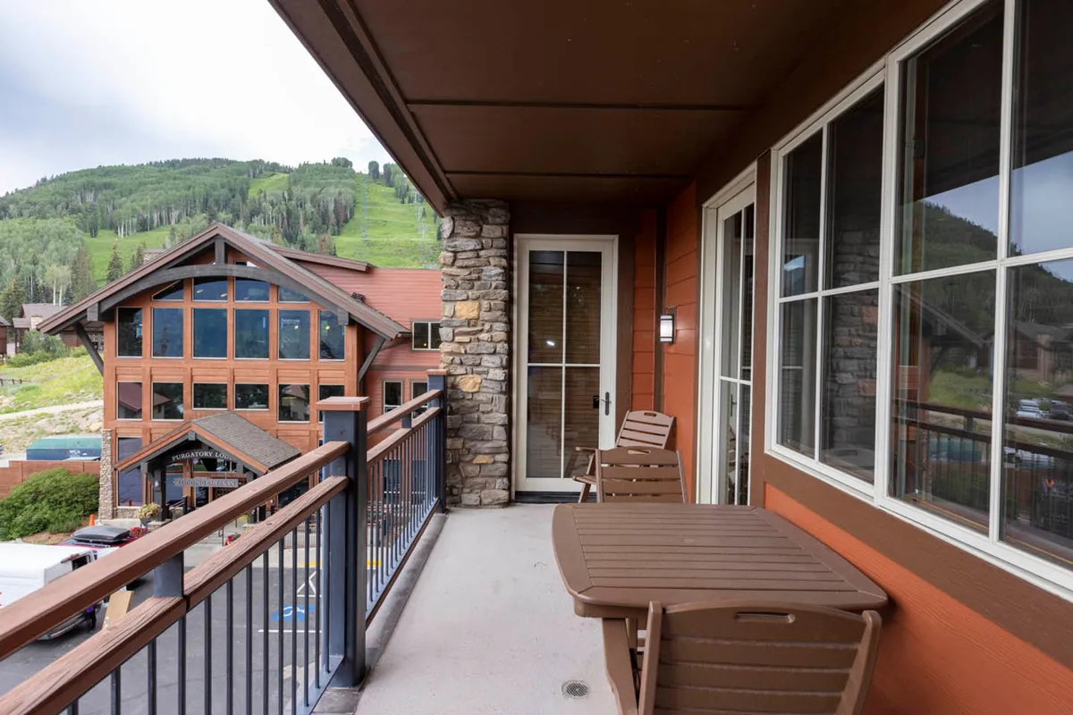 A serene balcony setup with comfortable outdoor furniture overlooking a spectacular mountain landscape. The balcony is designed for relaxation, socializing, or simply soaking in the panoramic views, with the building’s architectural details visible.