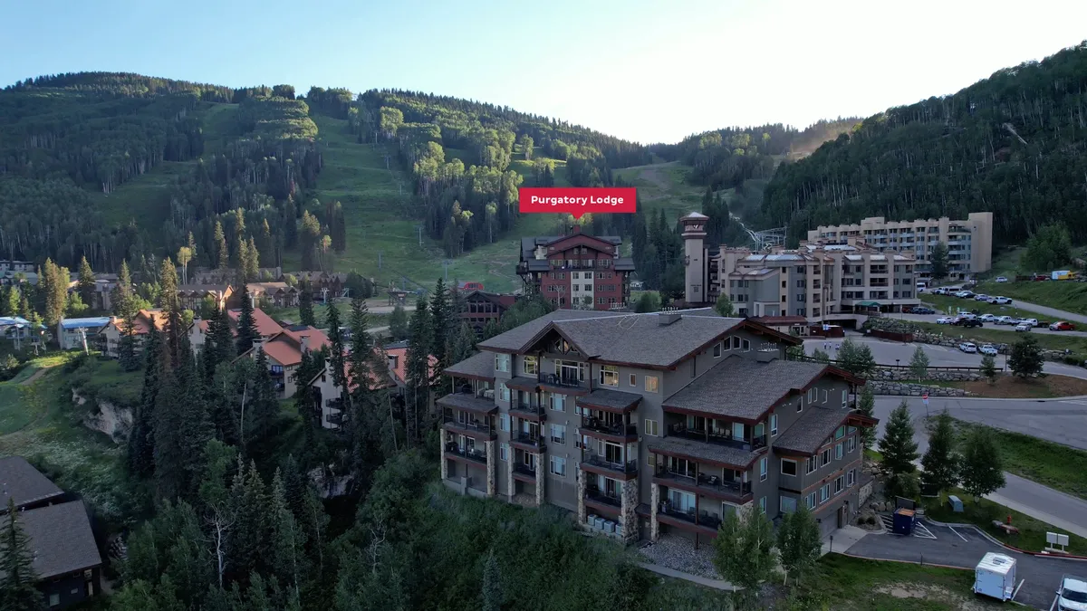 This image showcases the exterior of Purgatory Lodge nestled in the beautiful San Juan Mountains. The scene displays the lodge with the sweeping mountain backdrop and hints at the proximity to trails and outdoor activities. The mood is relaxed, capturing the mountain resort atmosphere.