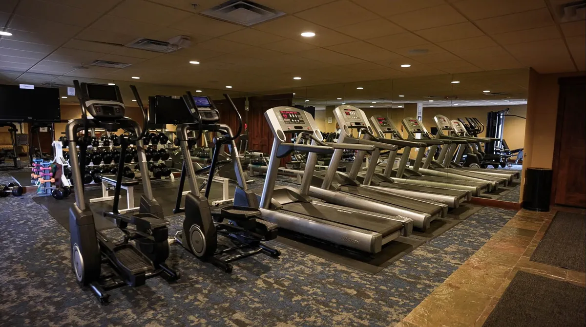 This energetic interior photo reveals the resort's fitness center, featuring a row of treadmills and ellipticals, dumbbells, and a mirrored wall for a modern, motivating workout space. The equipment is arranged to promote group workouts and solo training alike.